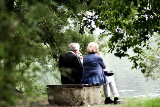 two people sitting on pavement facing on body of water by Sven Mieke courtesy of Unsplash.