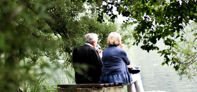 two people sitting on pavement facing on body of water by Sven Mieke courtesy of Unsplash.